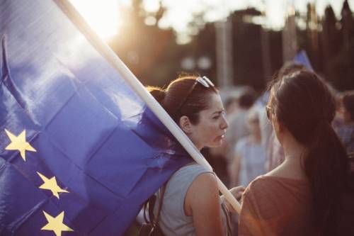 Zwei junge Frauen, eine hat eine Europaflagge geschultert.